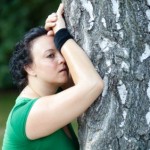 An overweight woman tired from jogging and leaning against a tree.