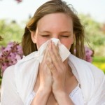 A woman in a field on a summer day, sneezing into a handkerchief.