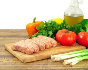 Five lamb sausages on a chopping board with a selection of vegetables.