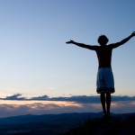 Arms outstretched on a sunset mountain.