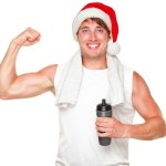 A man flexing his right bicep while holding a water bottle and wearing a Christmas hat.