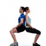 A man and a woman performing back to back partner squats.